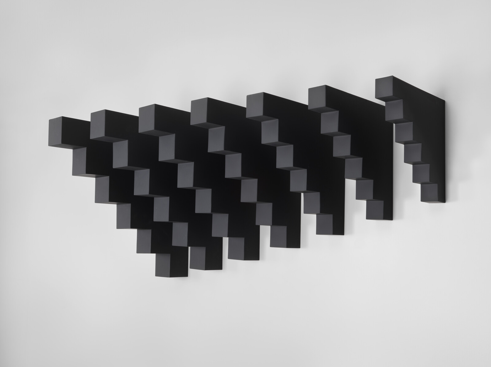 A black geometric wall sculpture of repeating stepped blocks forming a triangular wave pattern.