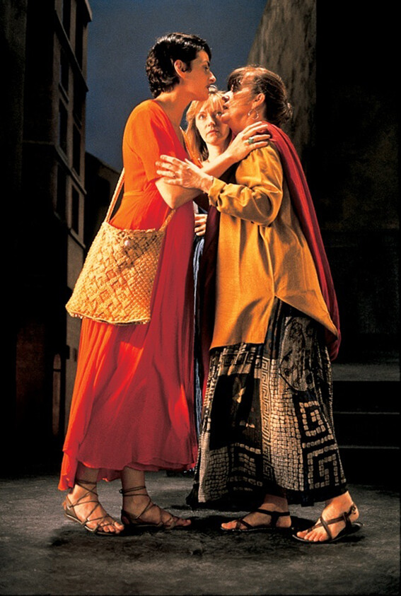 Two women lean in to touch foreheads while a third woman watches closely.