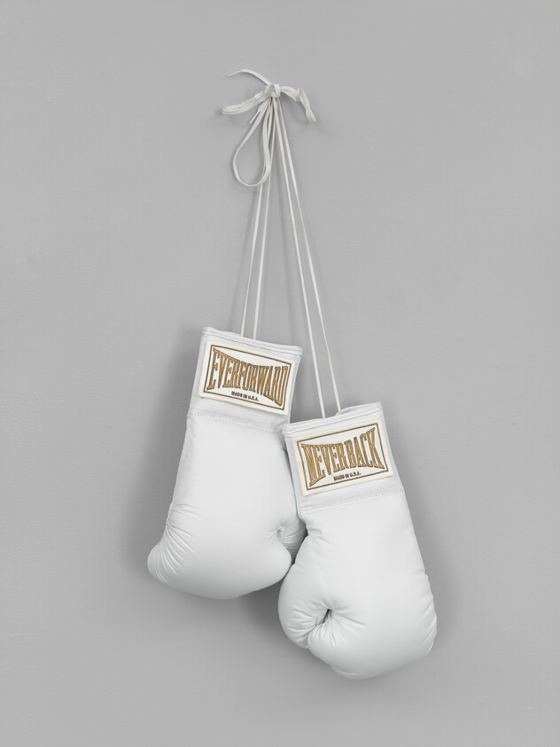 A pair of white boxing gloves hangs by their laces against a plain gray wall.