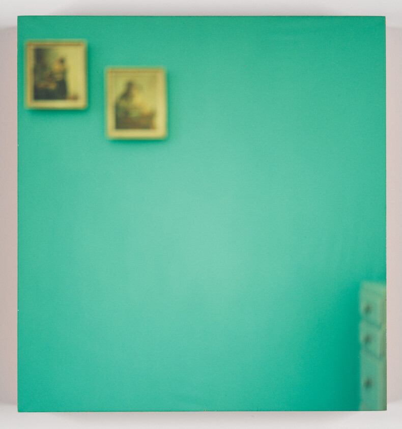 Teal wall with two small framed portraits at the top left and a partial dresser on the right.