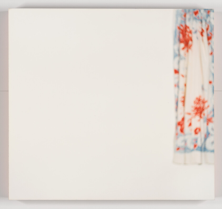 A large blank white canvas hangs on the wall with a floral curtain visible at right.