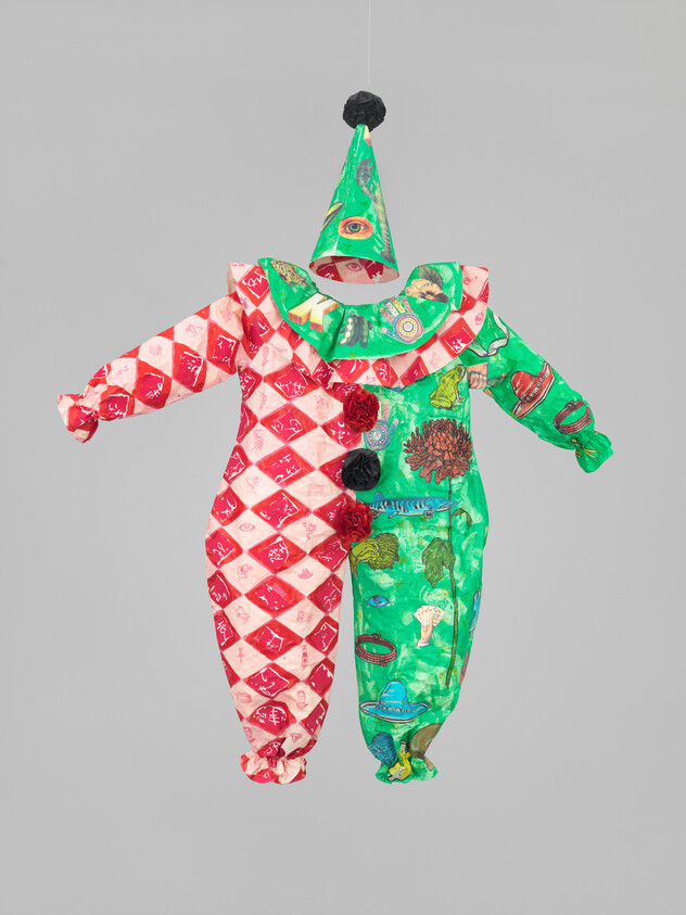 A hanging clown costume divided red-and-white diamond pattern and green printed fabric with pom-poms.