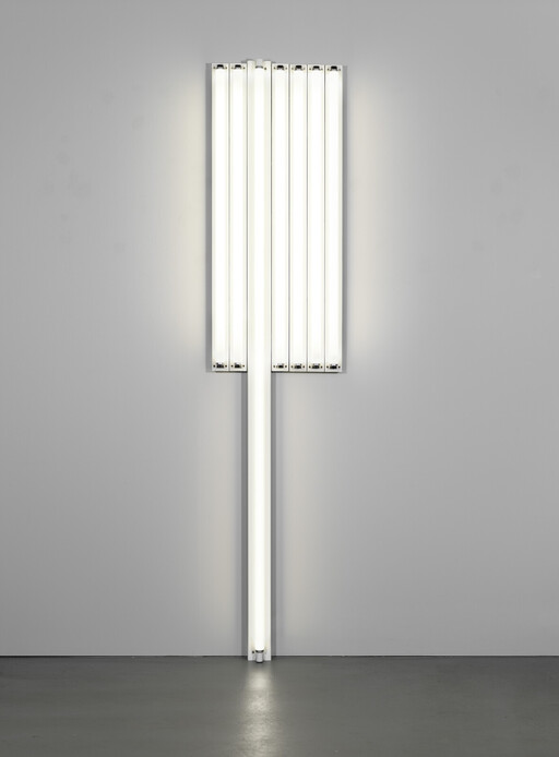 A tall vertical fluorescent light installation with multiple tubes mounted on a gray wall and floor.