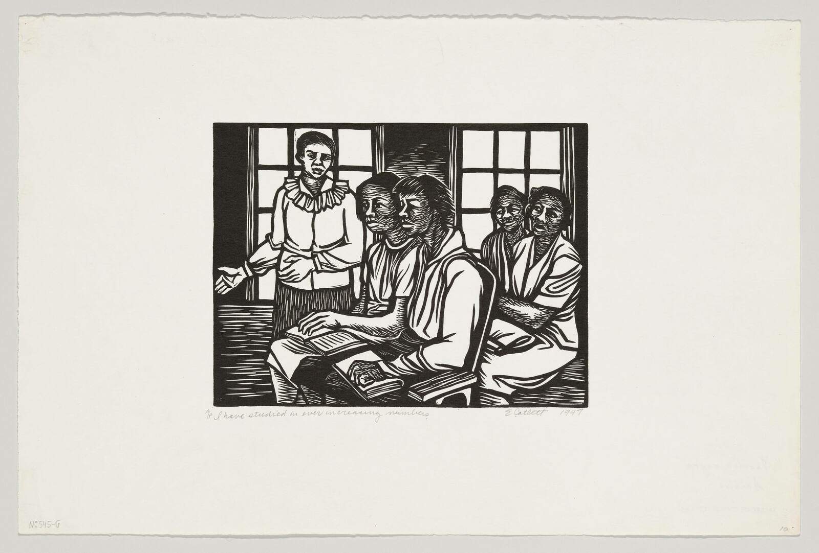 Four Black women sitting in a classroom with books on their laps while a standing woman lectures.