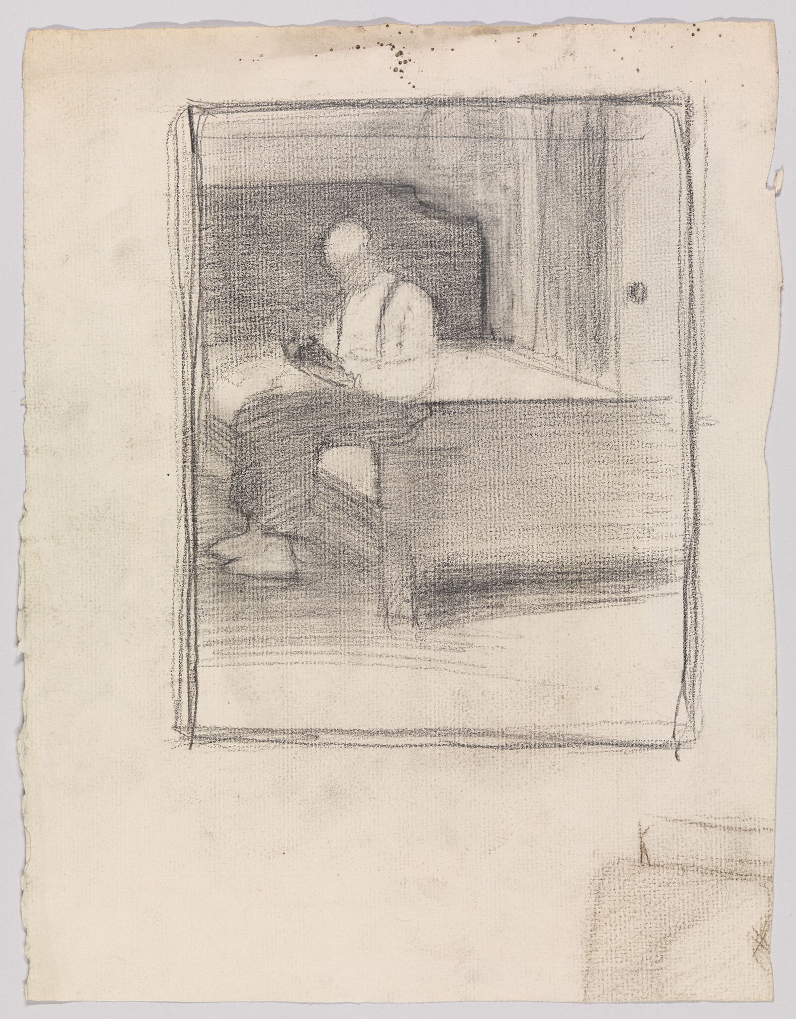 A person sits on the edge of a bed reading a small book in a dim room.