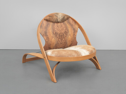 Low wooden lounge chair with curved frame and tan cowhide seat cushion.