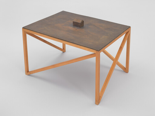 Square table with a dark top, light wooden legs, and a small block in the center of the surface.