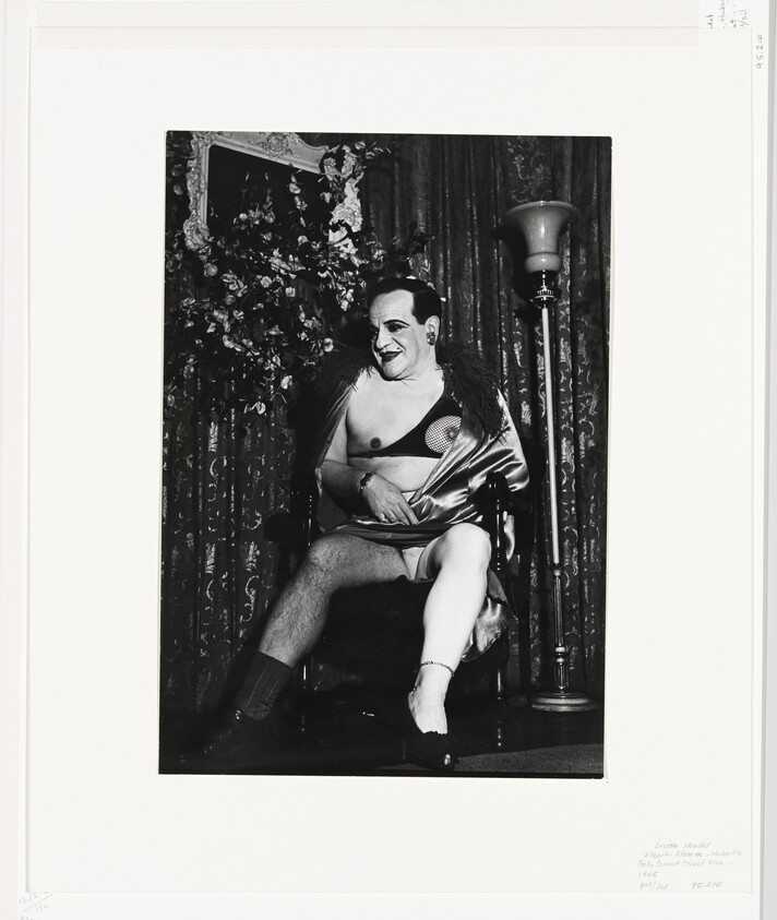 A seated person in partial lingerie and robe smiles while posing in a vintage room.