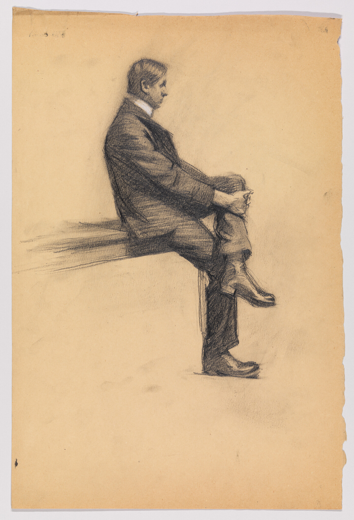 A man in a suit sits in profile with crossed legs, hands resting on his knee.