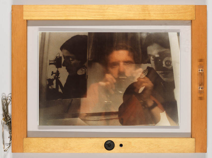 Reflected self-portraits of a person holding a camera and a tripod visible in a wooden frame.