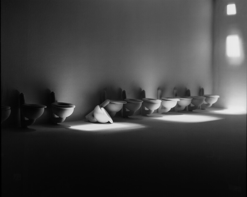 A row of wall-mounted toilets with one tipped over in a beam of light.