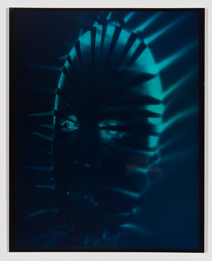 A face lit by teal light with striped shadows like window blinds.