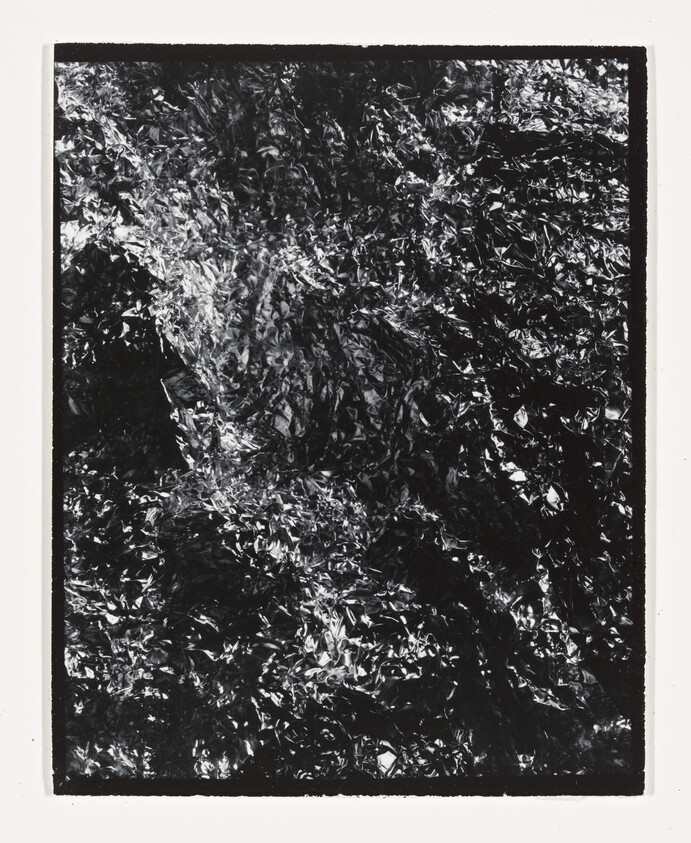 Crumpled reflective foil with shiny highlights filling a dark rectangular frame.