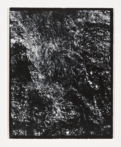 Crumpled reflective foil with shiny highlights filling a dark rectangular frame.