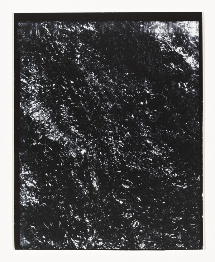 A framed sheet of crinkled black foil with reflective highlights and a white border.