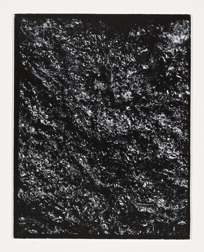 Crumpled black foil with shiny highlights inside a white rectangular border.