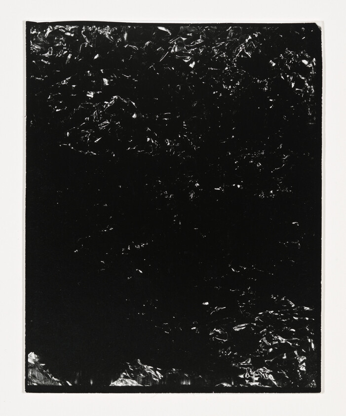 A dark rectangular sheet with a crinkled reflective surface centered on a white background.