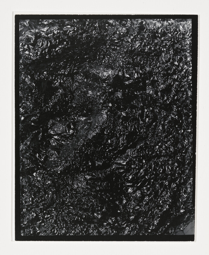 Crinkled shiny black plastic sheet framed by a white border, showing dense textured surface.
