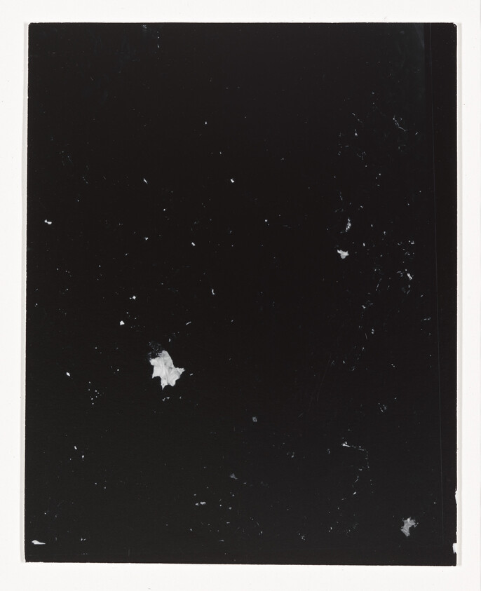 Black background with scattered white specks and a torn white paper fragment near the center.