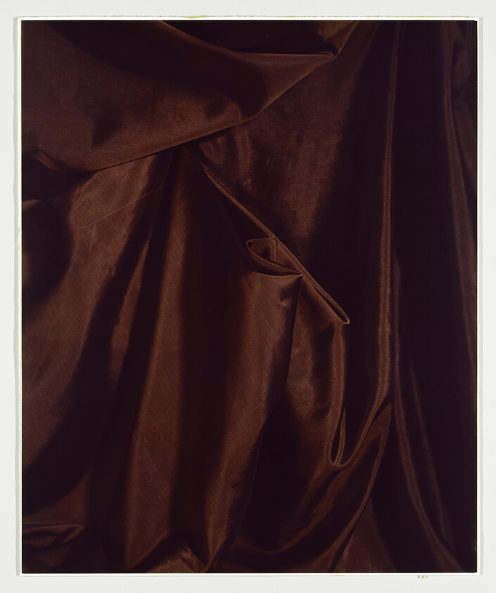 Dark brown satin fabric draped with soft folds and a small looped fold near center.