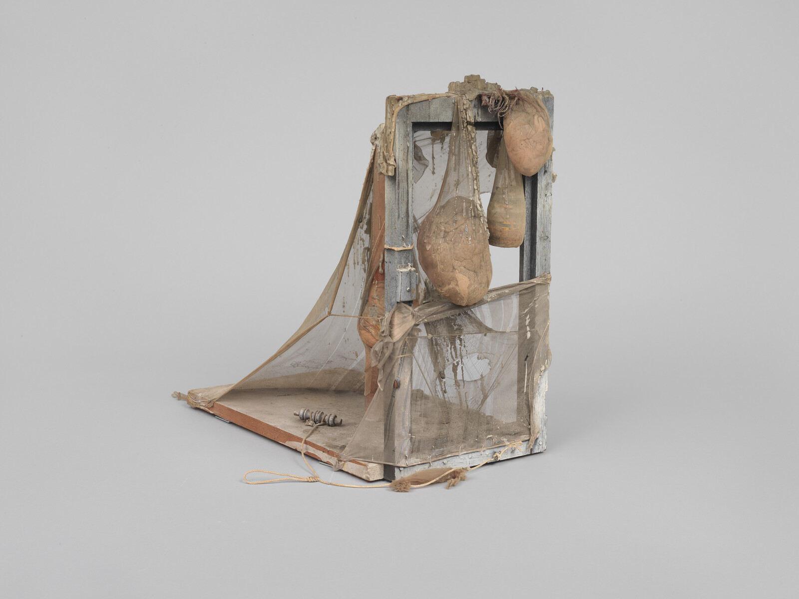 A small wooden frame draped with torn mesh netting and three hanging burlap sacks.