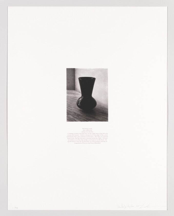 A dark ceramic vase sits on a wooden surface with small printed text beneath it.