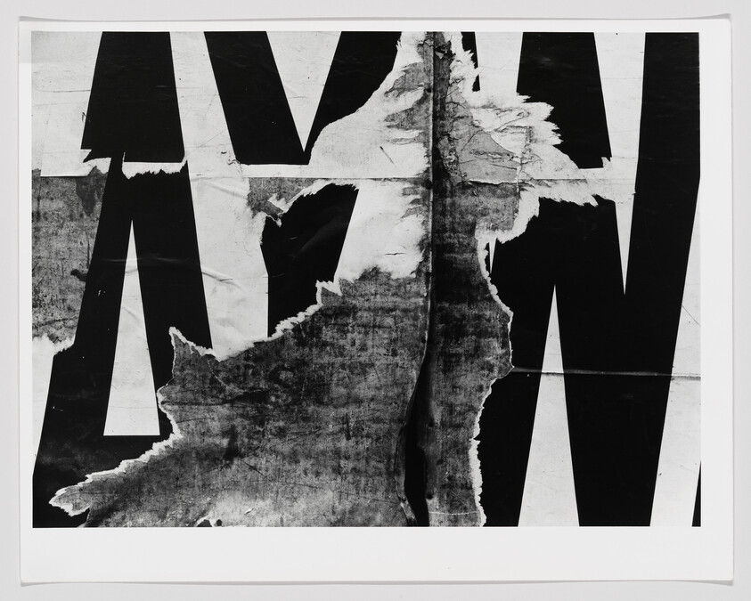 Large torn black letter posters layered and ripped down the center revealing textured paper beneath.