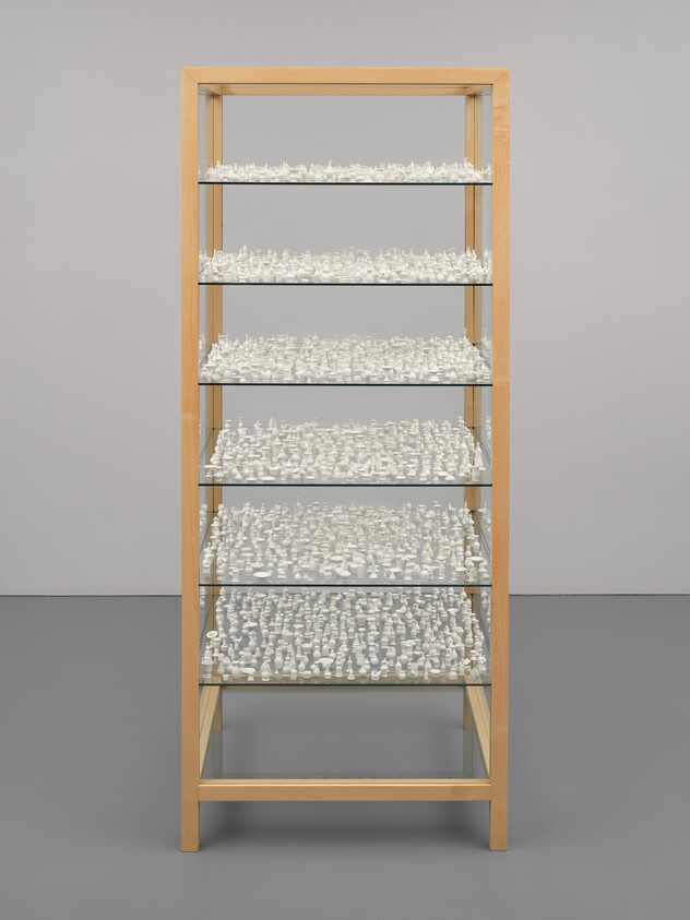 A wooden bookshelf with five shelves filled with numerous small white figurines against a gray background.