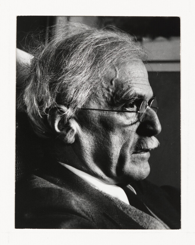 Elderly man with white hair and glasses in close-up profile, looking intently to the right.