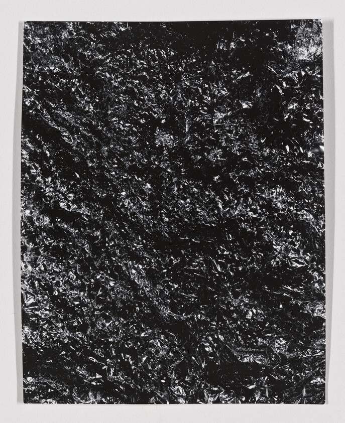 A rectangular sheet of crumpled black foil with shiny highlights on a white surface.