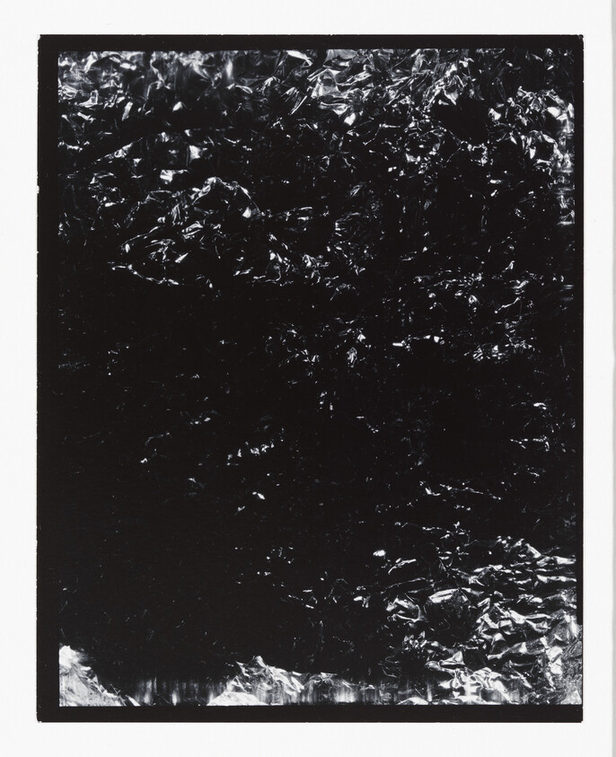 Crumpled reflective black foil fills a bordered rectangle, showing scattered bright highlights.