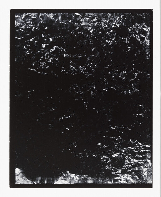 Crumpled reflective black foil fills a bordered rectangle, showing scattered bright highlights.