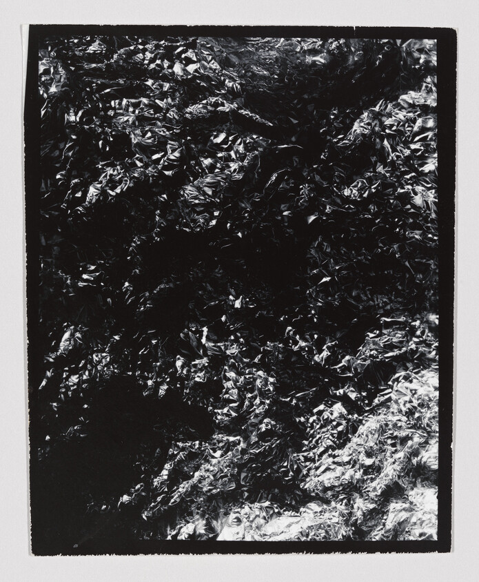 Crumpled metallic foil with dark and bright highlights fills a rectangular white-bordered frame.