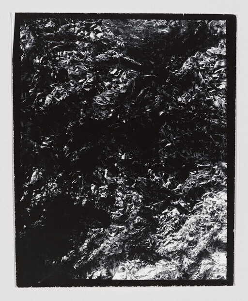 Crumpled metallic foil with dark and bright highlights fills a rectangular white-bordered frame.