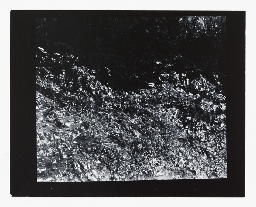 Crumpled reflective aluminum foil creating chaotic light and dark textures across the frame.