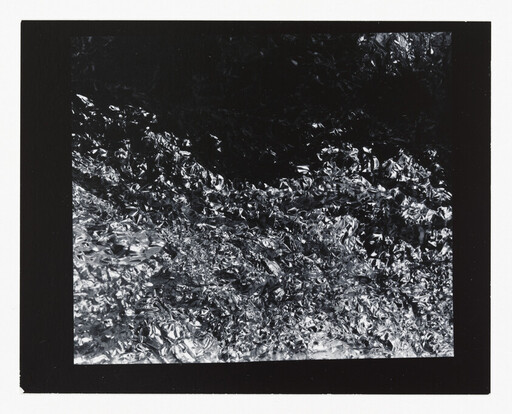 Crumpled reflective aluminum foil creating chaotic light and dark textures across the frame.