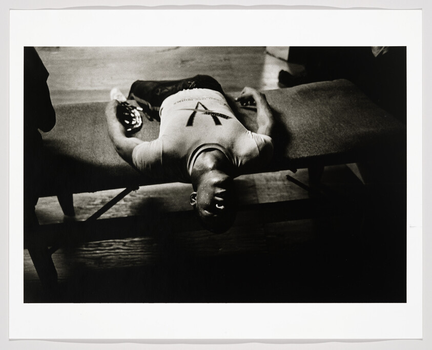 Man lies on a gym bench with his head hanging off and arms relaxed at his sides.