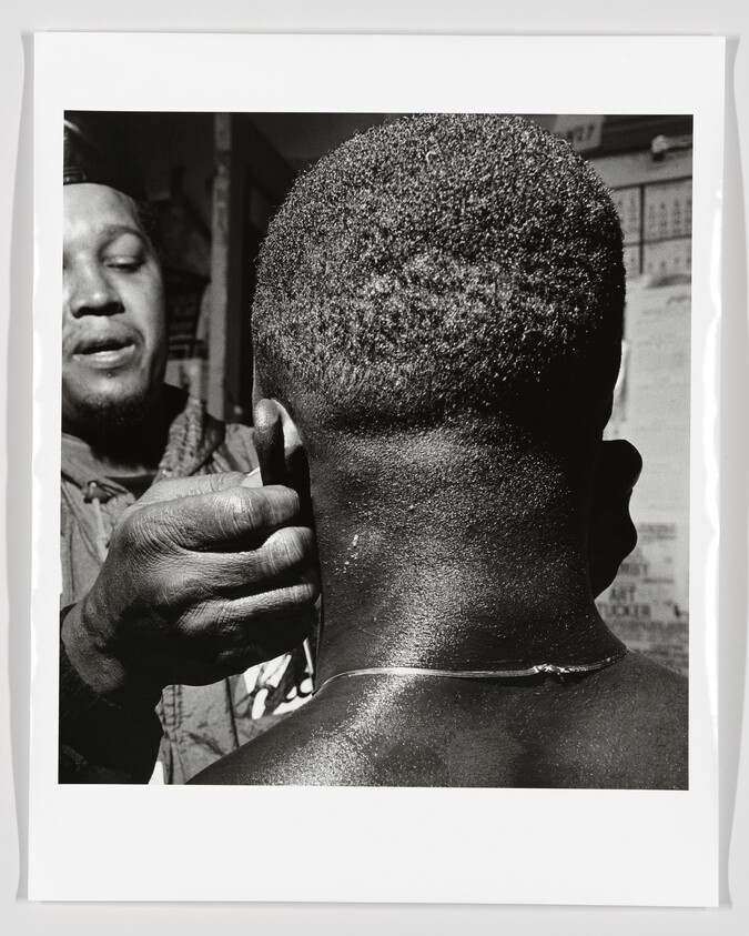 A barber adjusts a young man's ear while giving a close haircut at a shop.