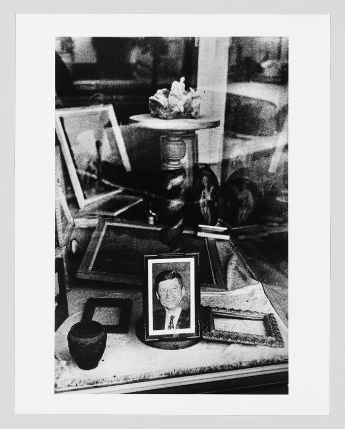 A framed portrait of a man sits among empty picture frames and decorative objects in a shop window.