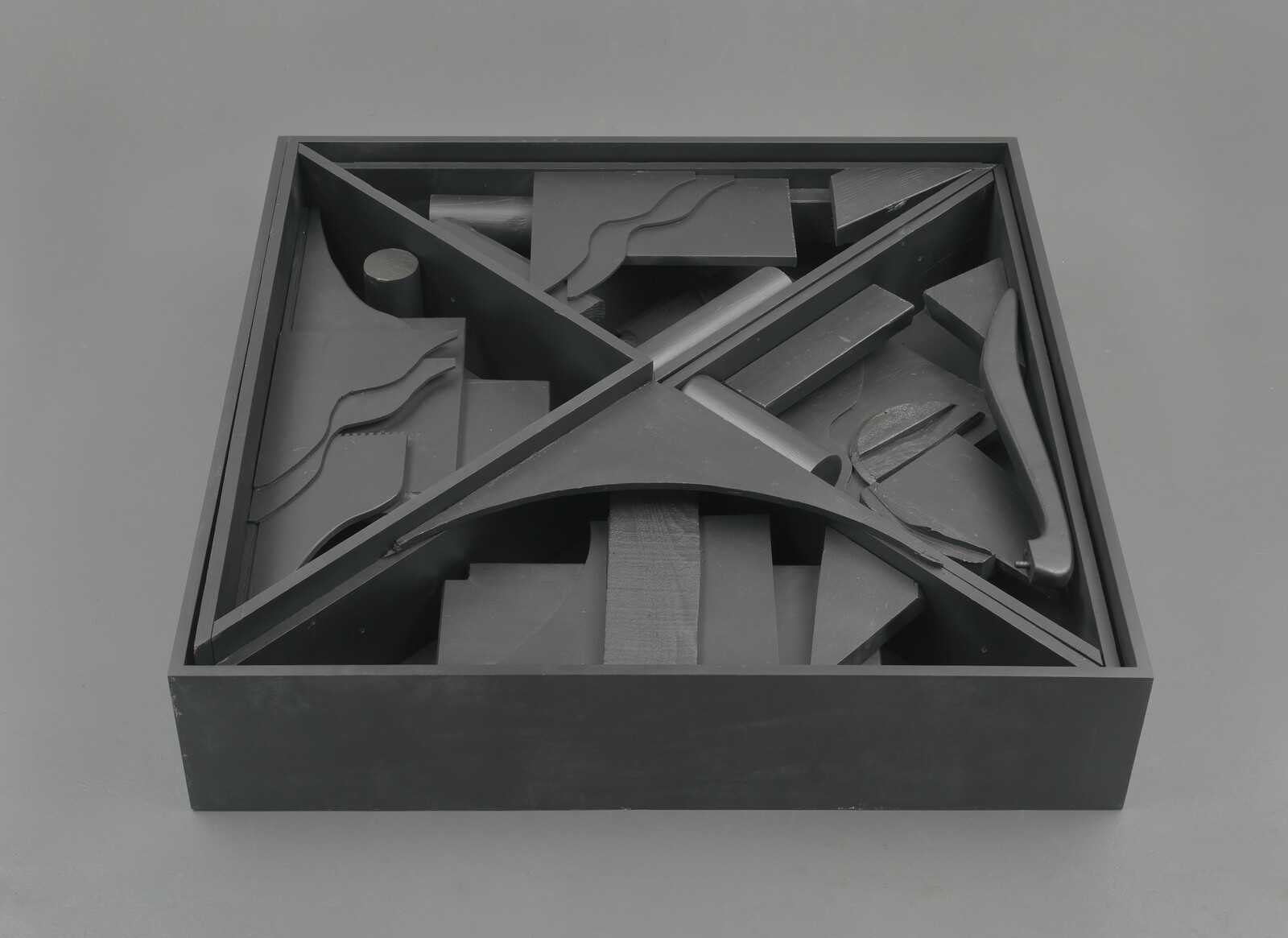 A shallow black square box holds abstract geometric shapes arranged in four triangular compartments.