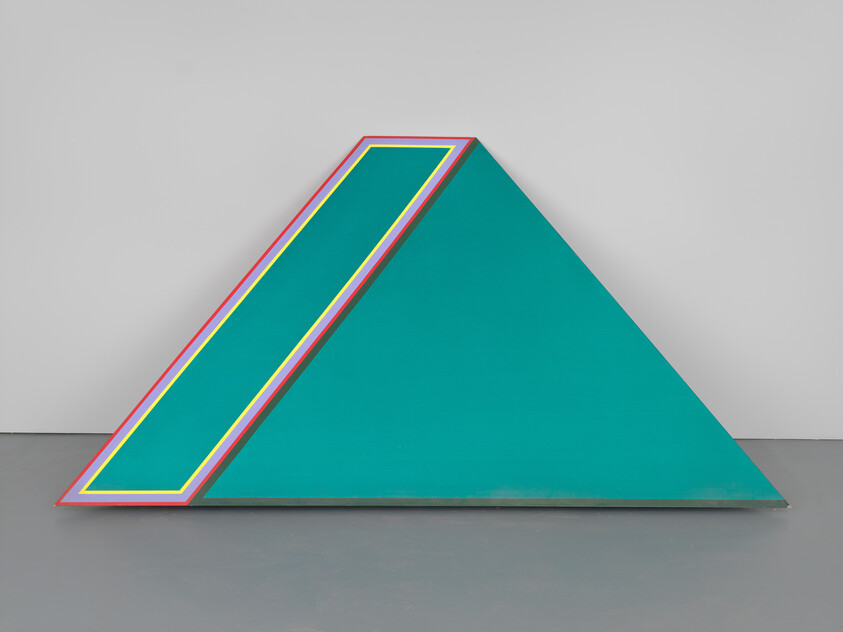 A large teal triangular sculpture leans against a wall with a diagonal multicolored stripe panel.