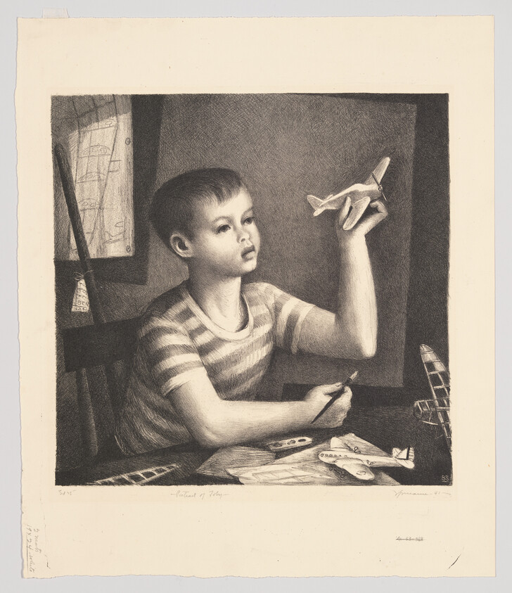 A young boy holds a toy airplane aloft while working on model planes at a table.