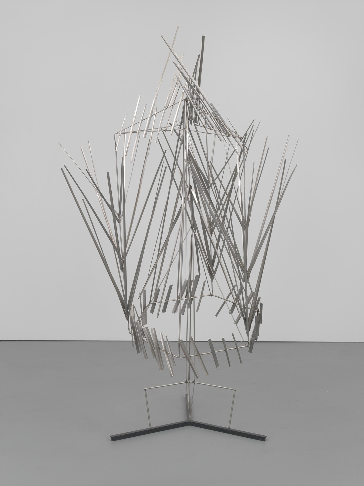 A tall abstract metal sculpture composed of thin rods forming angular, feather-like shapes on a three-legged base.
