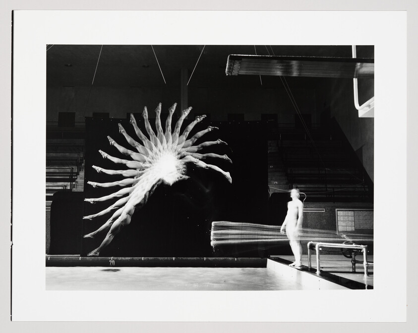 A diver captured in multiple exposures forms a twisting arc of bodies above the pool while a second person watches.