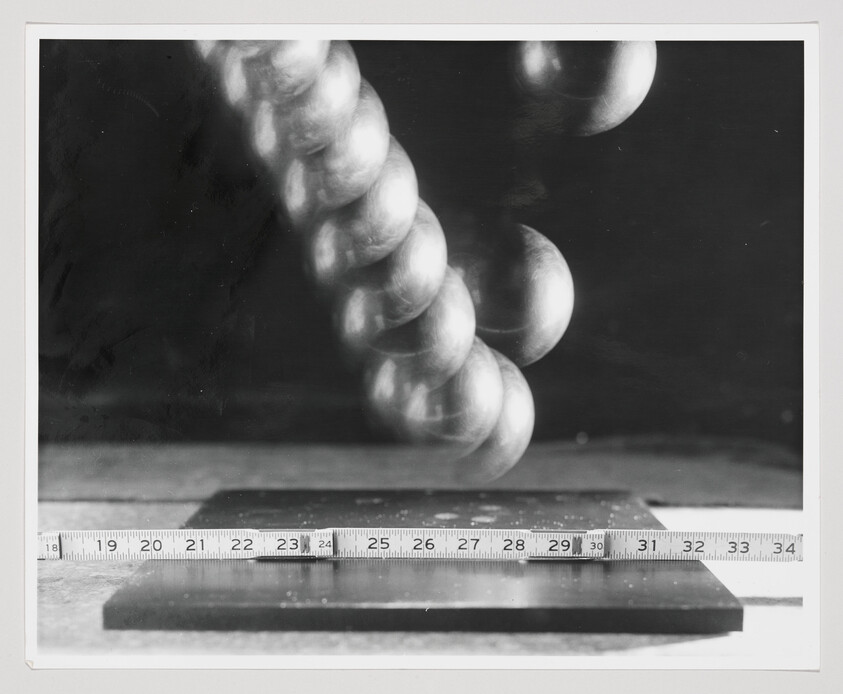 A sequence of a metal ball falling and bouncing above a ruler and flat surface.