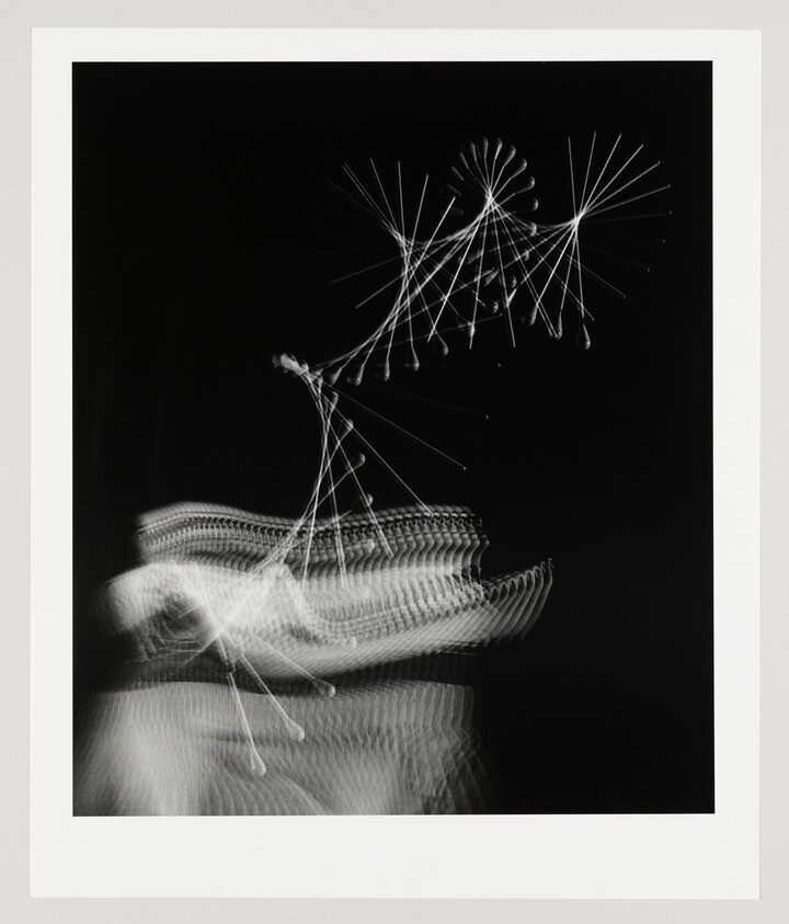 Blurred white light trails form abstract fan and wave shapes against a black background.