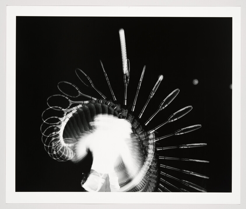 Figure spinning illuminated hoops creates radiating light arcs against a dark background.