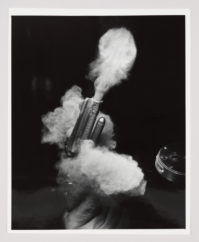 Hand holding a small pistol as thick smoke billows from its barrel.