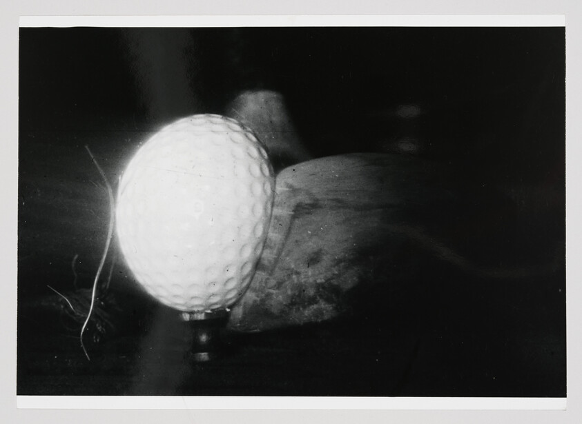 A golf ball teed up in front of a wooden club head, ready to be struck.