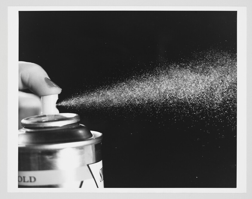 Hand presses an aerosol spray can and releases a fine mist into the air.